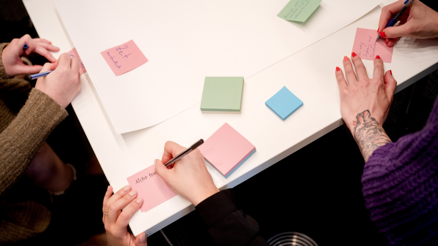 Hände schreiben etwas auf Post-It-Zettel